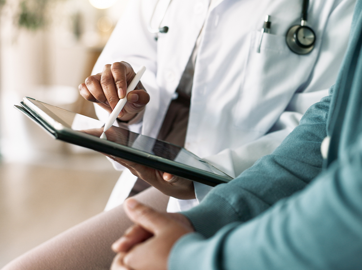 Doctor using a digital tablet with a stylus while consulting with a patient.